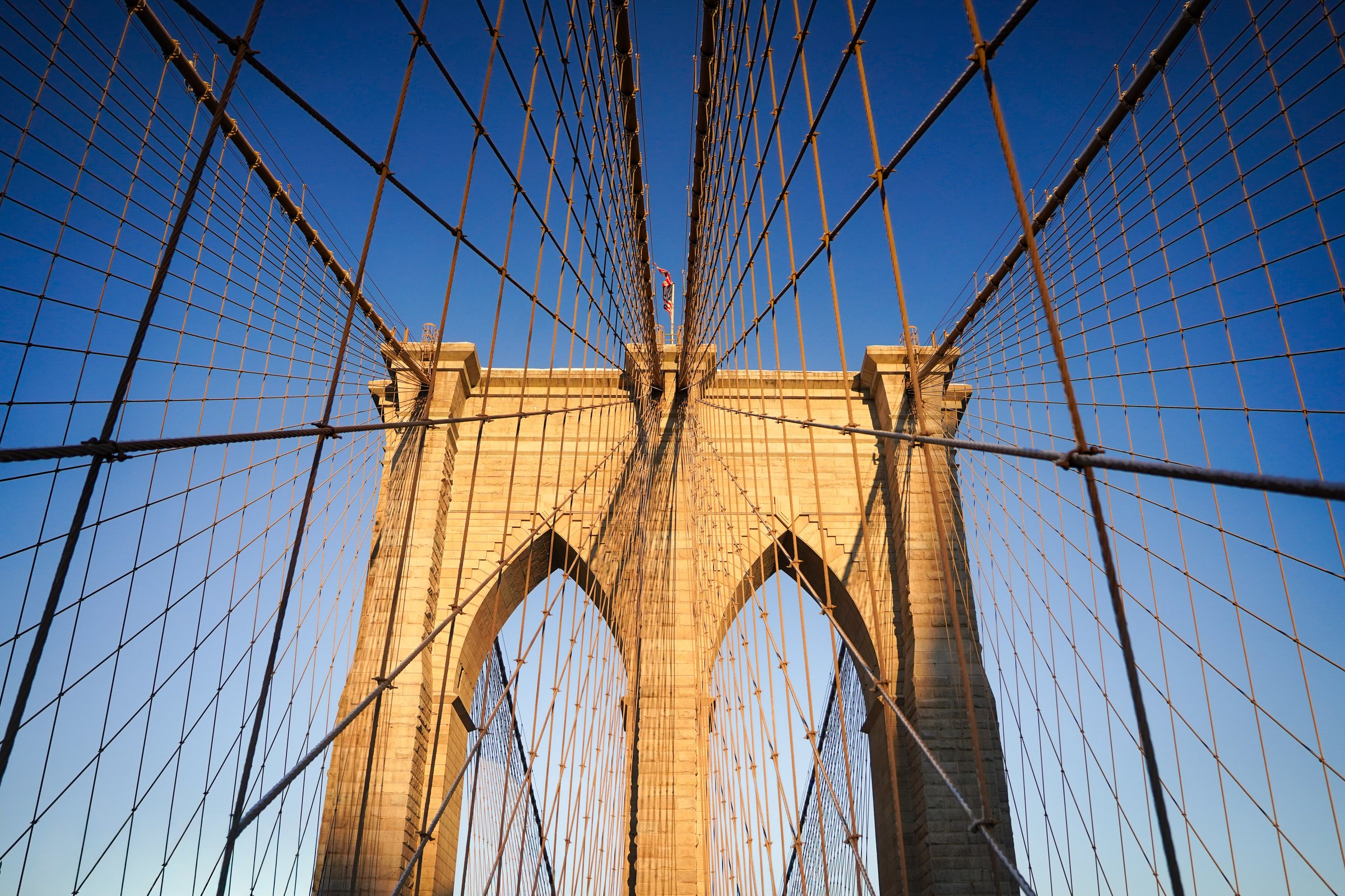 Brooklyn Bridge tower close-up, dramatic cable geometry against blue sky